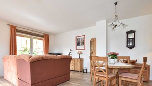 Een gezellige woonkamer met een bank, een houten eettafel, stoelen en een televisie.
