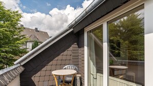 A balcony with a table and chair, a window, and a view of trees and a house. - Inviting Holiday Home in Winterberg-Hildfeld near Ski Slopes (Winterberg)