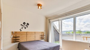 A bedroom with a bed, a wooden headboard, a wall-mounted lamp, a window with a view of the outdoors, and a balcony with a table. - Inviting Holiday Home in Winterberg-Hildfeld near Ski Slopes (Winterberg)