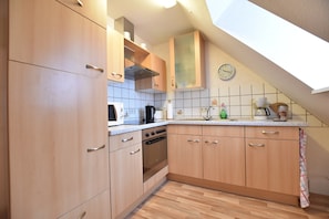A kitchen with wooden cabinets, a stove, a microwave, and a clock on the wall.