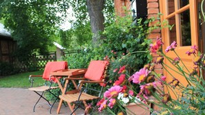 An outdoor seating area with wooden chairs and a table, surrounded by flowering plants and a brick wall. - Landhaus in Gressow mit Terrasse (Gaegelow)