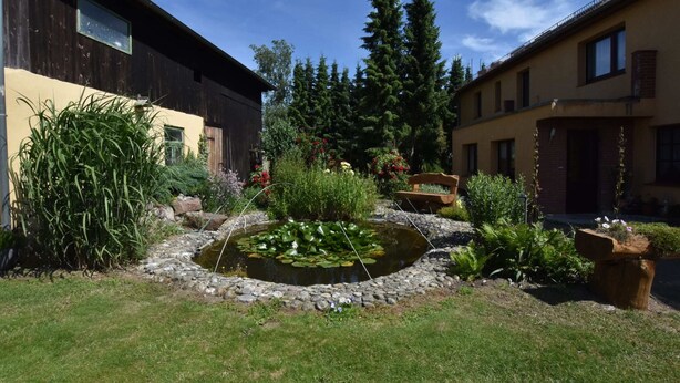 A courtyard with a pond, various plants, and two buildings with wooden facades. - Einladende Ferienwohnung in Zweedorf mit Grill (Bastorf)