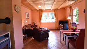 A cozy living room with a sofa, a dining table with chairs, a TV, and a window with curtains. - Einladende Ferienwohnung in Zweedorf mit Grill (Bastorf)