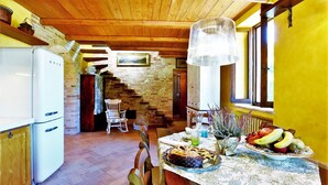 A rustic kitchen with a wooden ceiling, a white refrigerator, and a dining table set with fruits and a vase. - Elegant Villa in Montecosaro Italy with Hot Tub (Montecosaro)