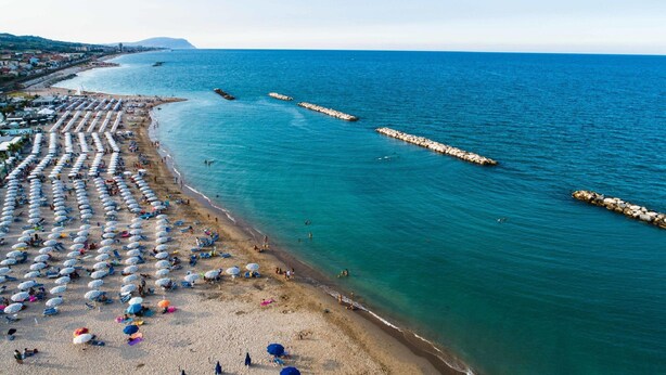 A beach with rows of umbrellas and sun loungers, a rocky breakwater, and calm sea. - Elegant Villa in Montecosaro Italy with Hot Tub (Montecosaro)
