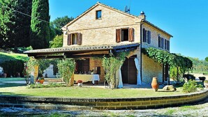 A two-story stone house with a covered patio, a garden with a fountain, and a large vase. - Elegant Villa in Montecosaro Italy with Hot Tub (Montecosaro)
