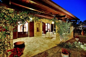 A covered outdoor patio with a brick wall, white chairs, and a table. - Elegant Villa in Montecosaro Italy with Hot Tub (Montecosaro)