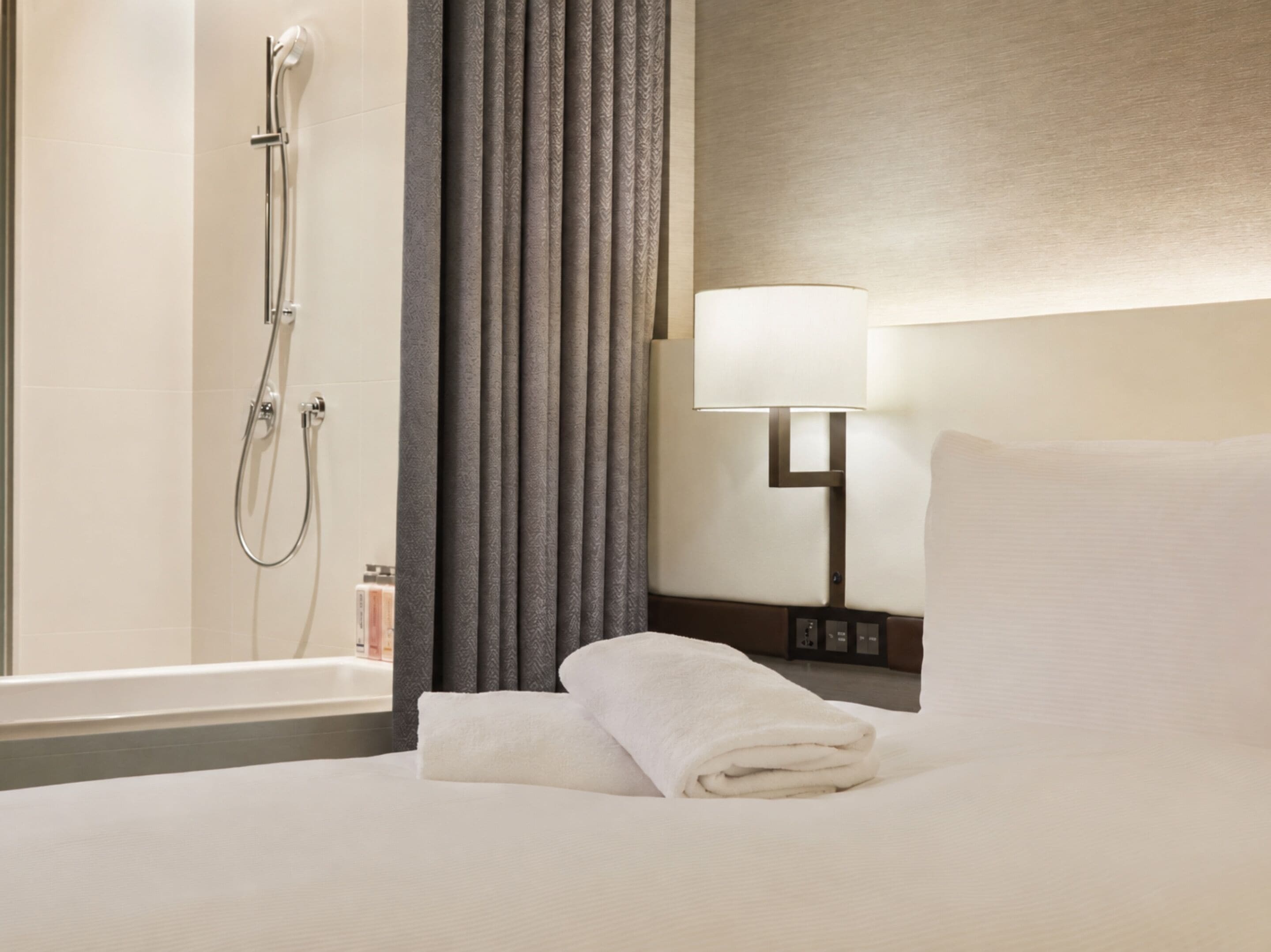Habitación de hotel con cama, baño con ducha, lámpara y cortina.