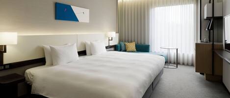 A hotel room with a large bed, a seating area with a sofa and a small table, and a television on a wooden stand.