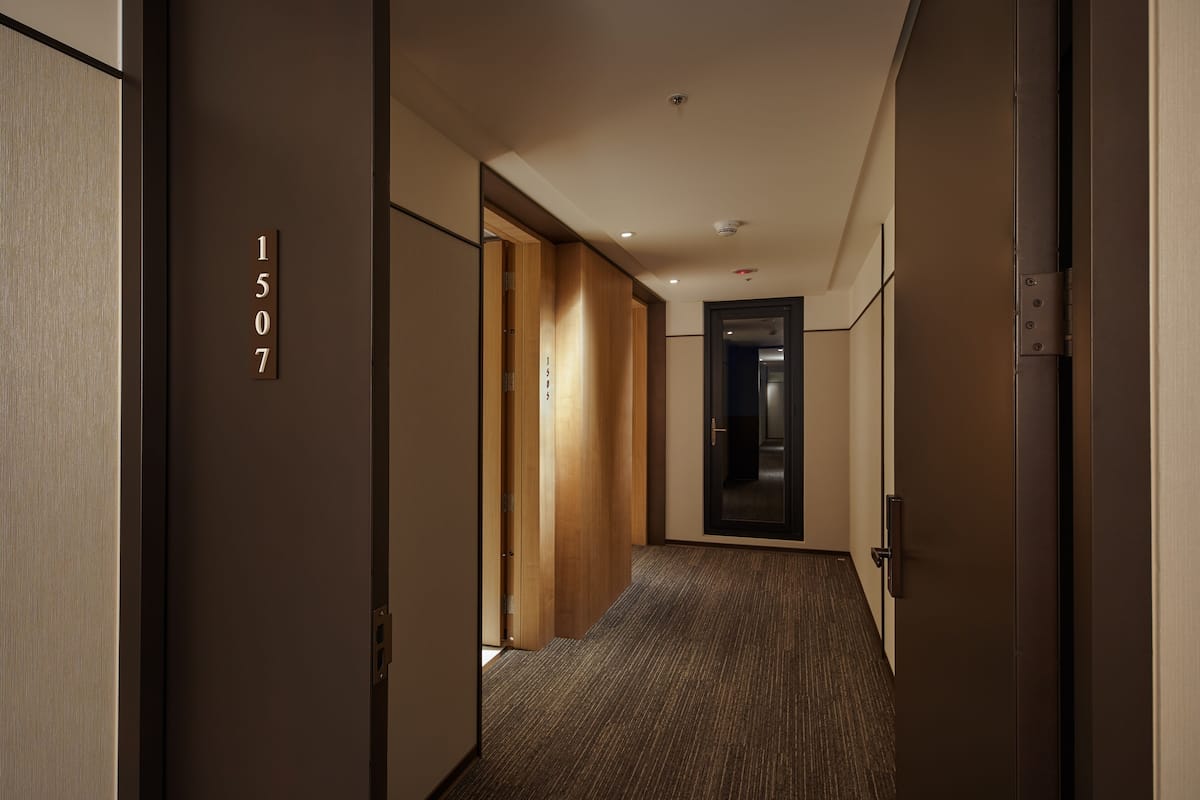 A hallway with a wooden door labeled "1507", a carpeted floor, and a modern ceiling design.