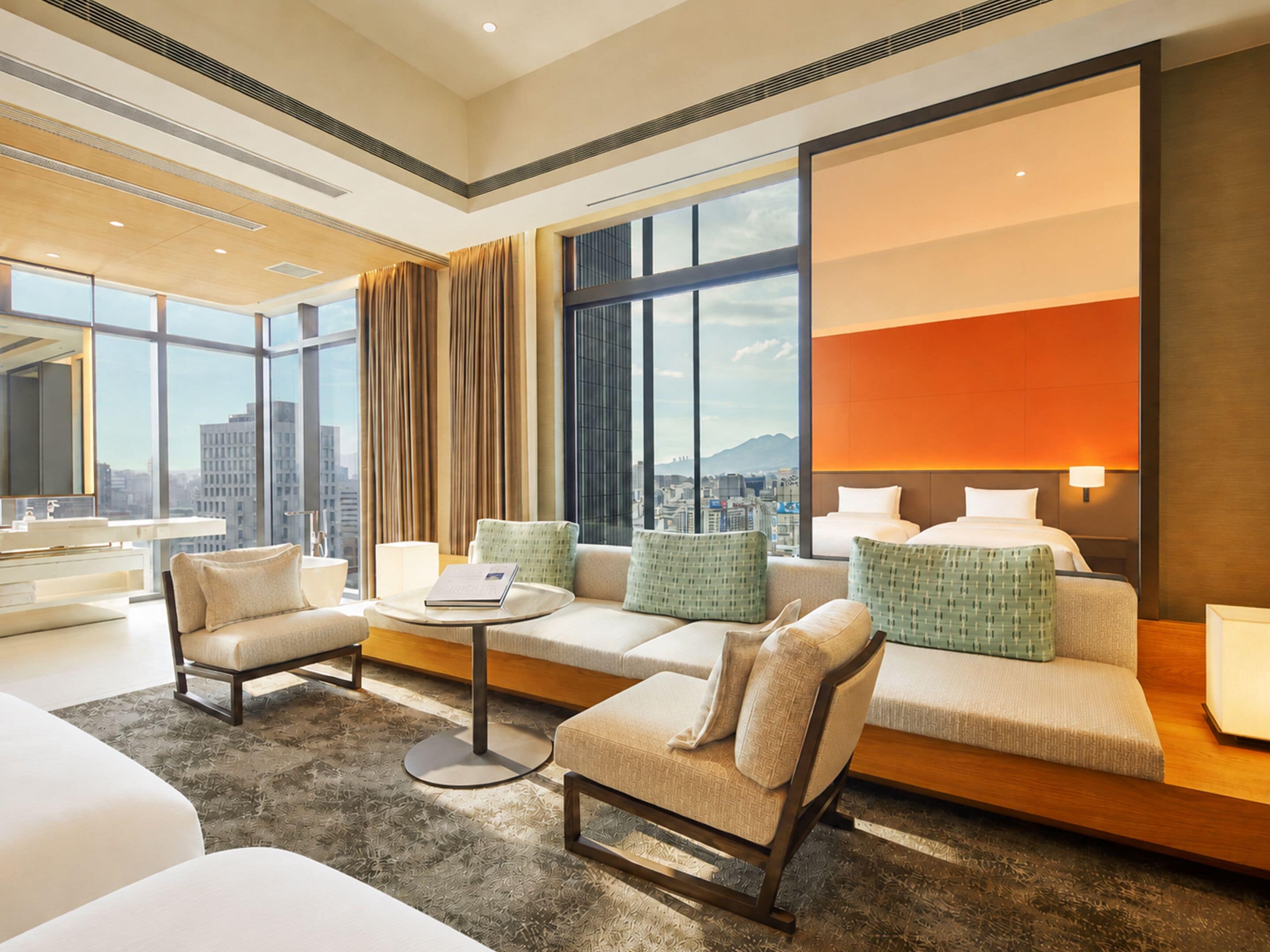 A modern hotel room with a sofa set, a round coffee table, and a large window offering a city view.