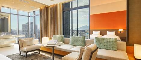 A modern hotel room with a sofa set, a round coffee table, and a large window offering a city view.