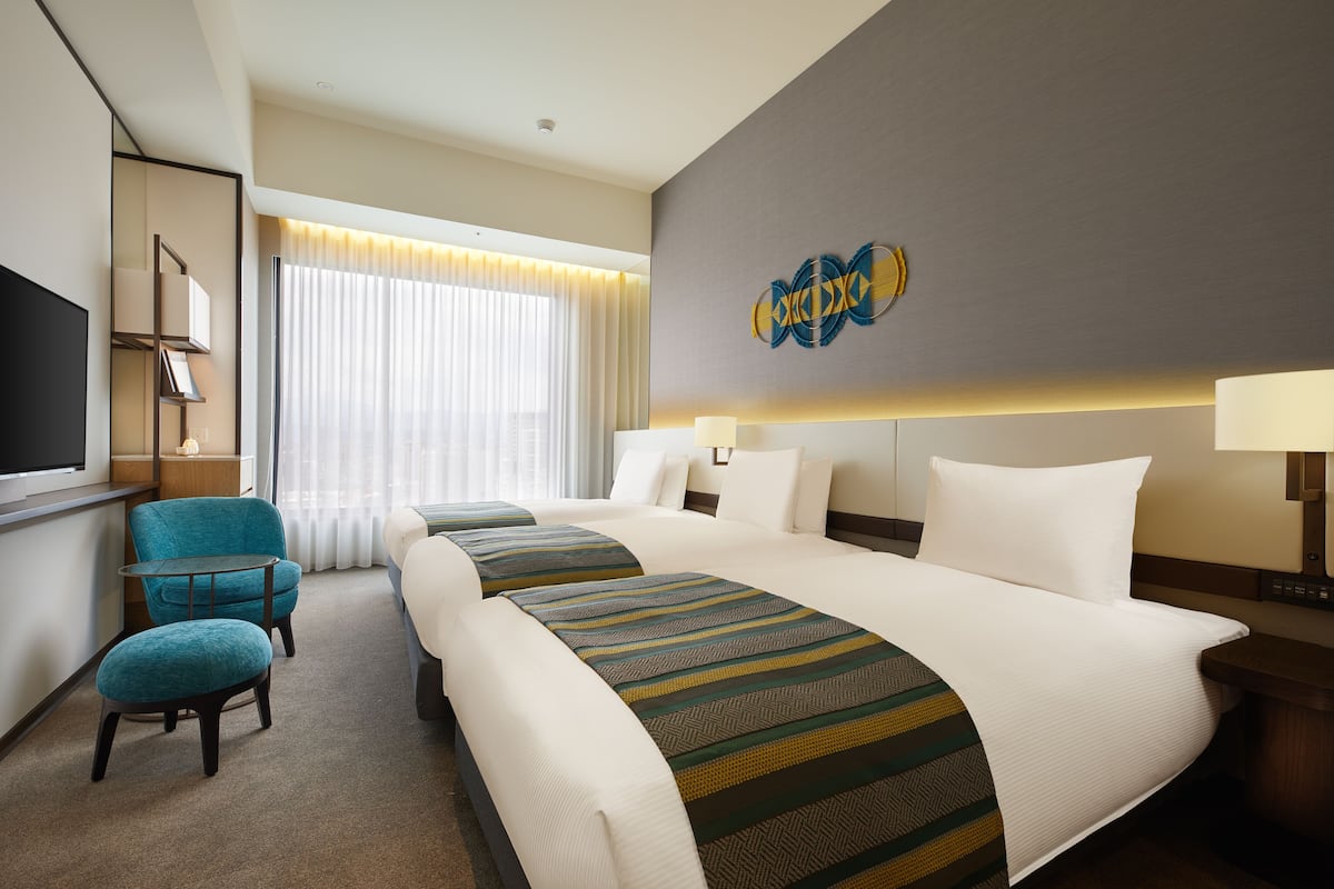 A hotel room with two beds, a TV, a desk, and a chair.