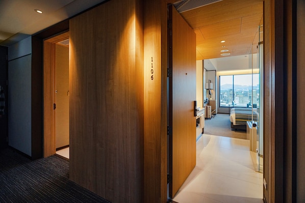 Un pasillo de hotel con paredes de madera, un número de habitación visible '1106', y una vista parcial de un dormitorio con cama y vista a la ciudad.