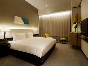 A hotel room with a large bed, bedside tables, a chair, a small table, and a TV.