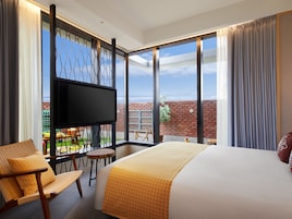 Een hotelkamer met een groot bed, een flatscreen televisie, een balkon met uitzicht en een zithoek met stoelen.