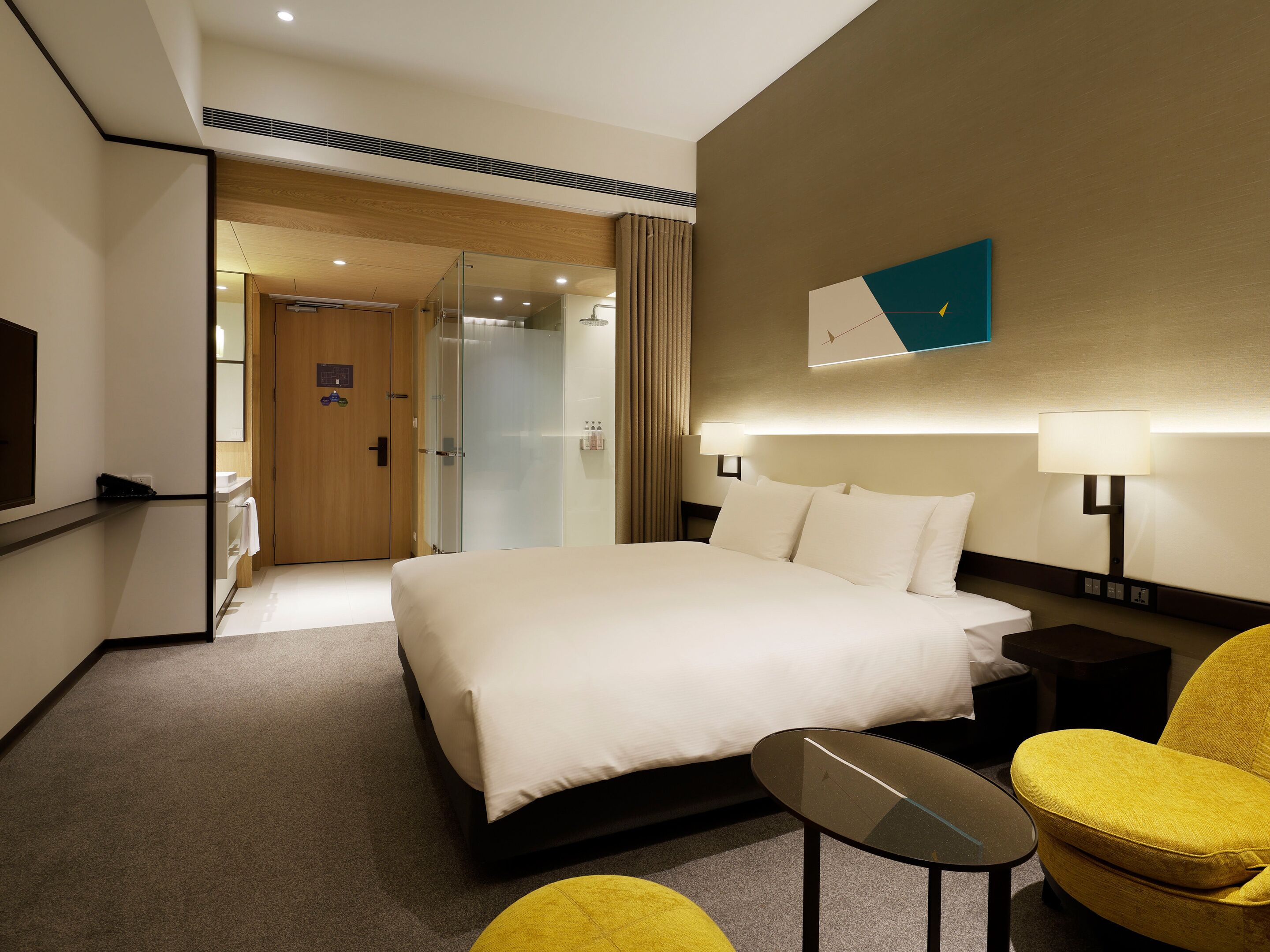 A hotel room with a large bed, a glass-enclosed shower, a flat-screen TV, and a small table.