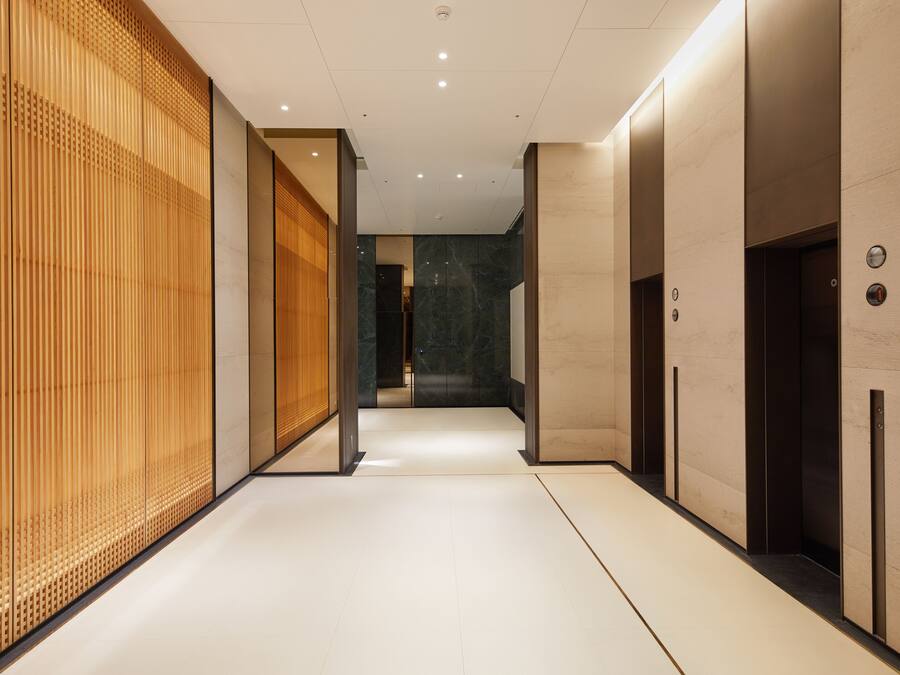 A modern hallway with a wooden panel wall, a marble floor, and an elevator on the right.