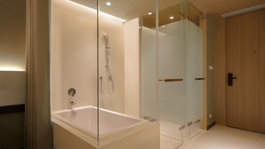 A modern bathroom with a glass-enclosed shower, a standalone bathtub, and a wooden door.