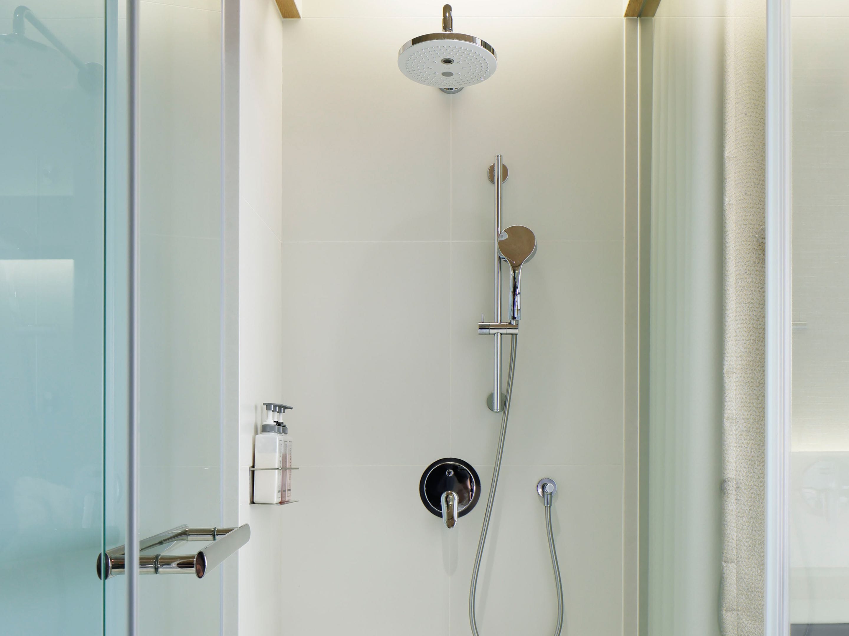 A modern shower with a handheld showerhead, a wall-mounted faucet, and a control panel.