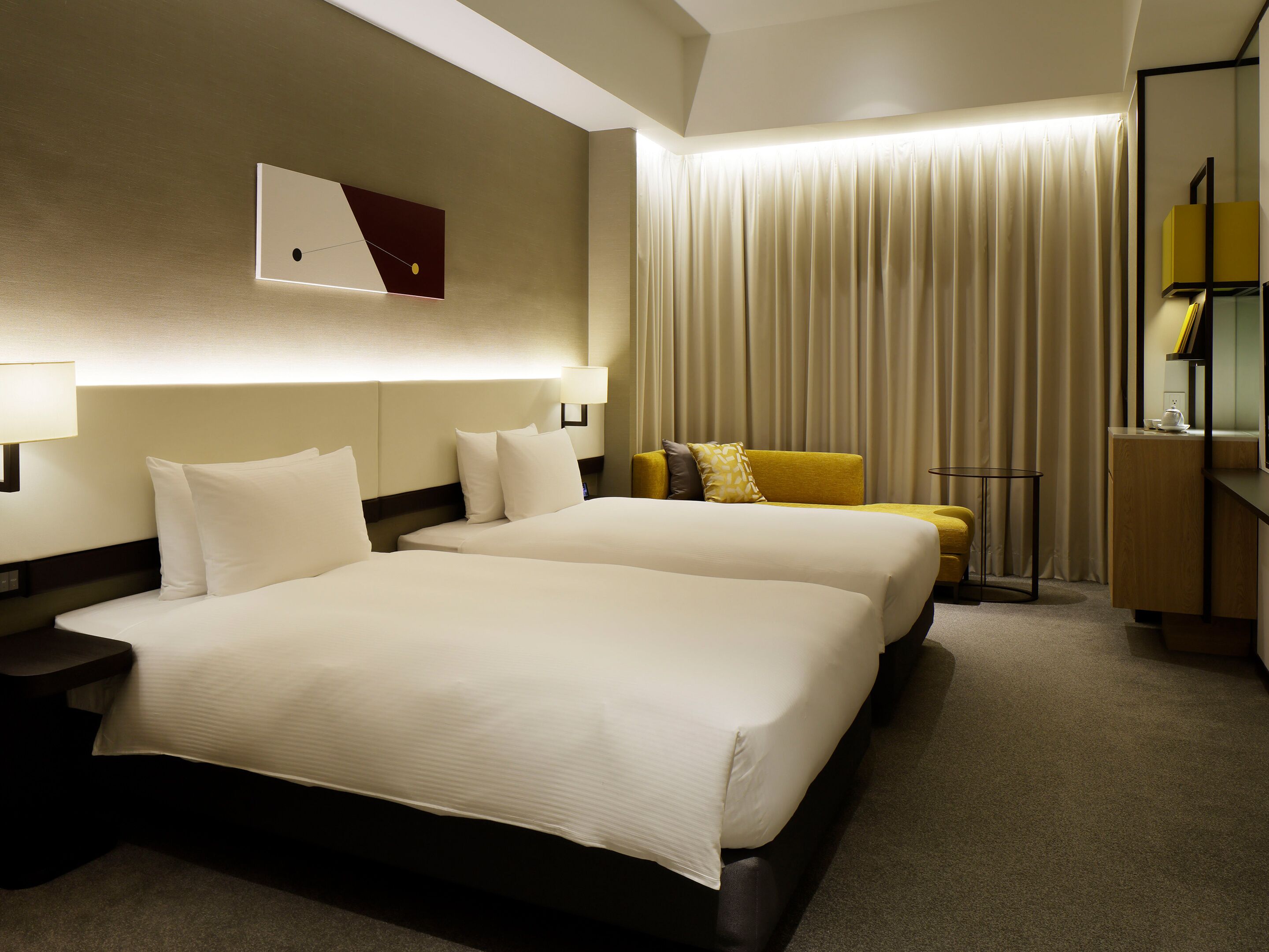 A hotel room with two beds, a desk, a chair, a lamp, and a curtain.