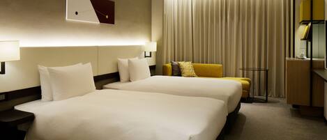 A hotel room with two beds, a desk, a chair, a lamp, and a curtain.