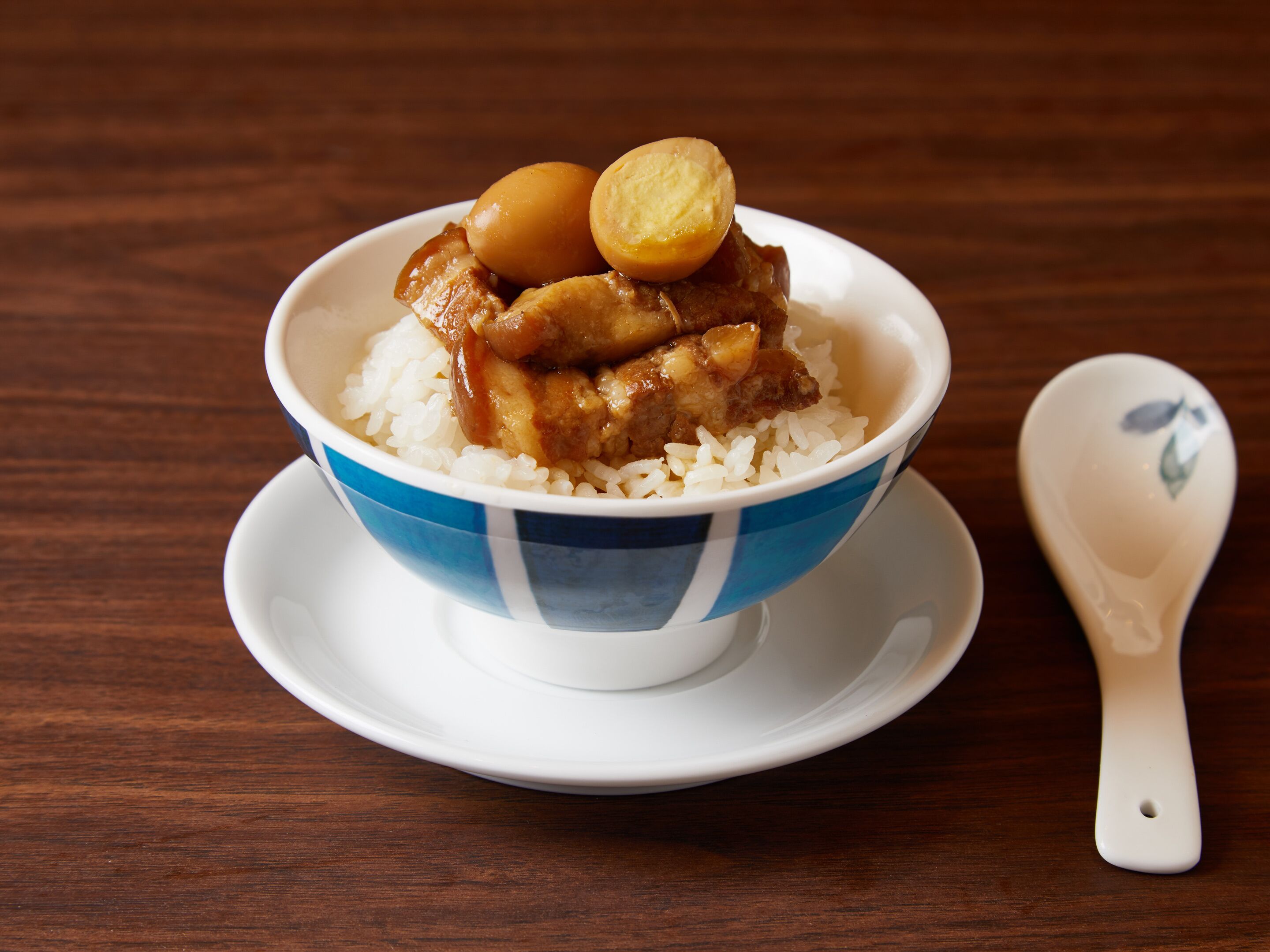 A bowl of rice with meat and a boiled egg on a wooden table.