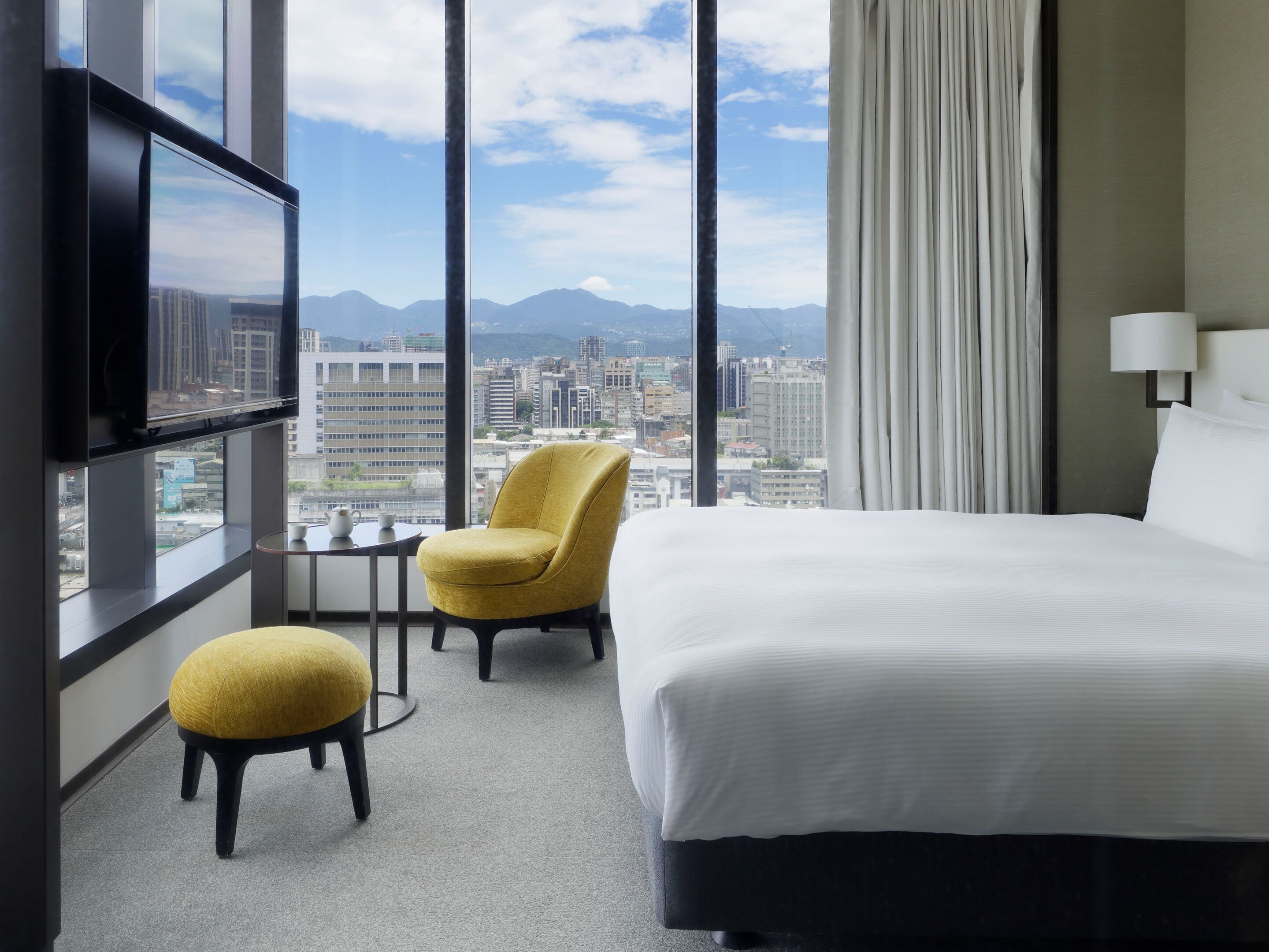 A hotel room with a bed, a chair, a small table, and a TV.