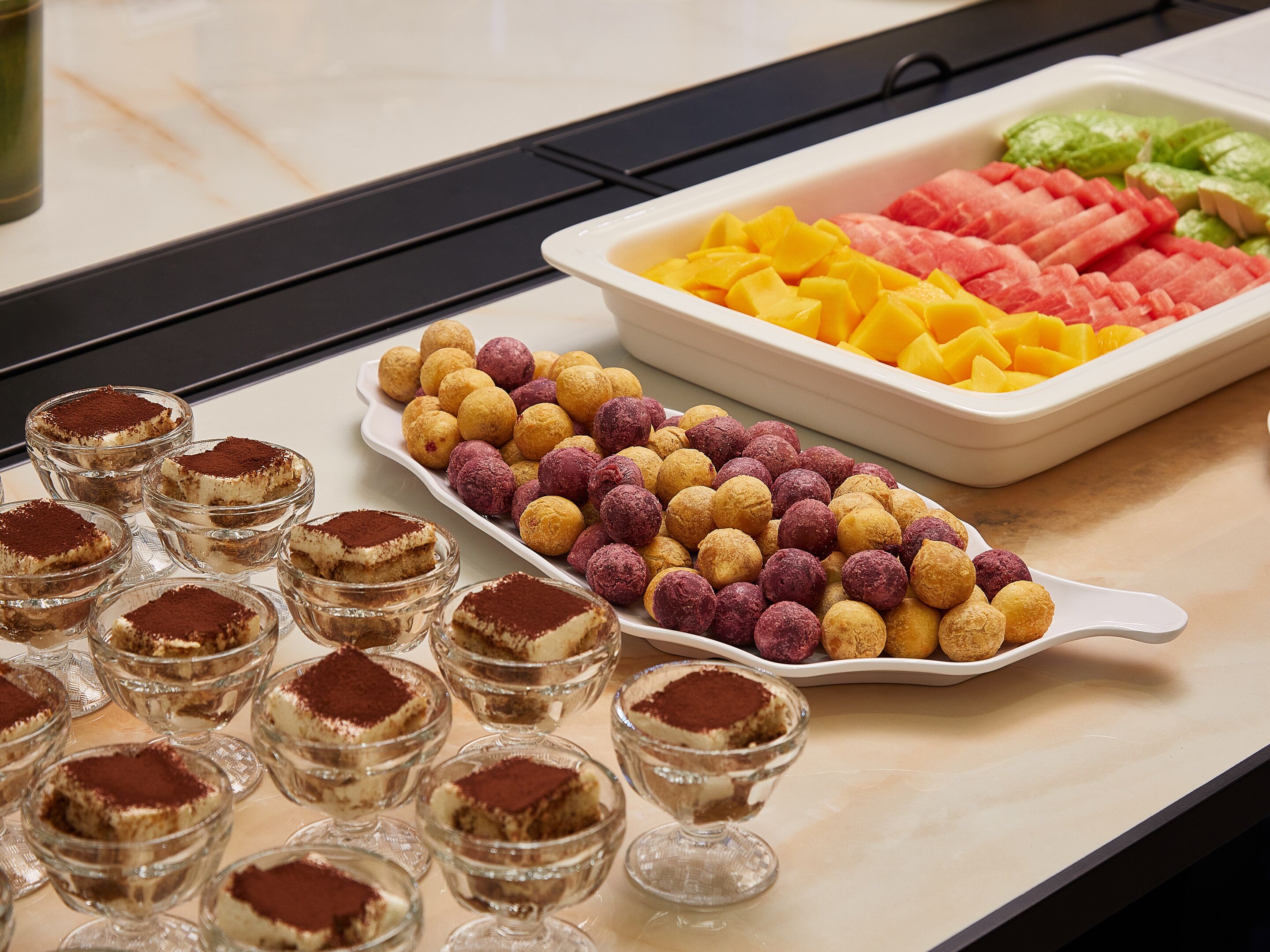 A buffet table with various food items including desserts and fruits.