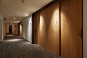 Un pasillo de hotel con puertas de madera, piso alfombrado e iluminación empotrada.
