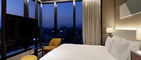 A hotel room with a large bed, a television, a chair, and a view of the cityscape.