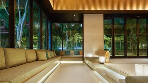 Un interior moderno con un sofá, una mesa y vistas a árboles a través de ventanas amplias.