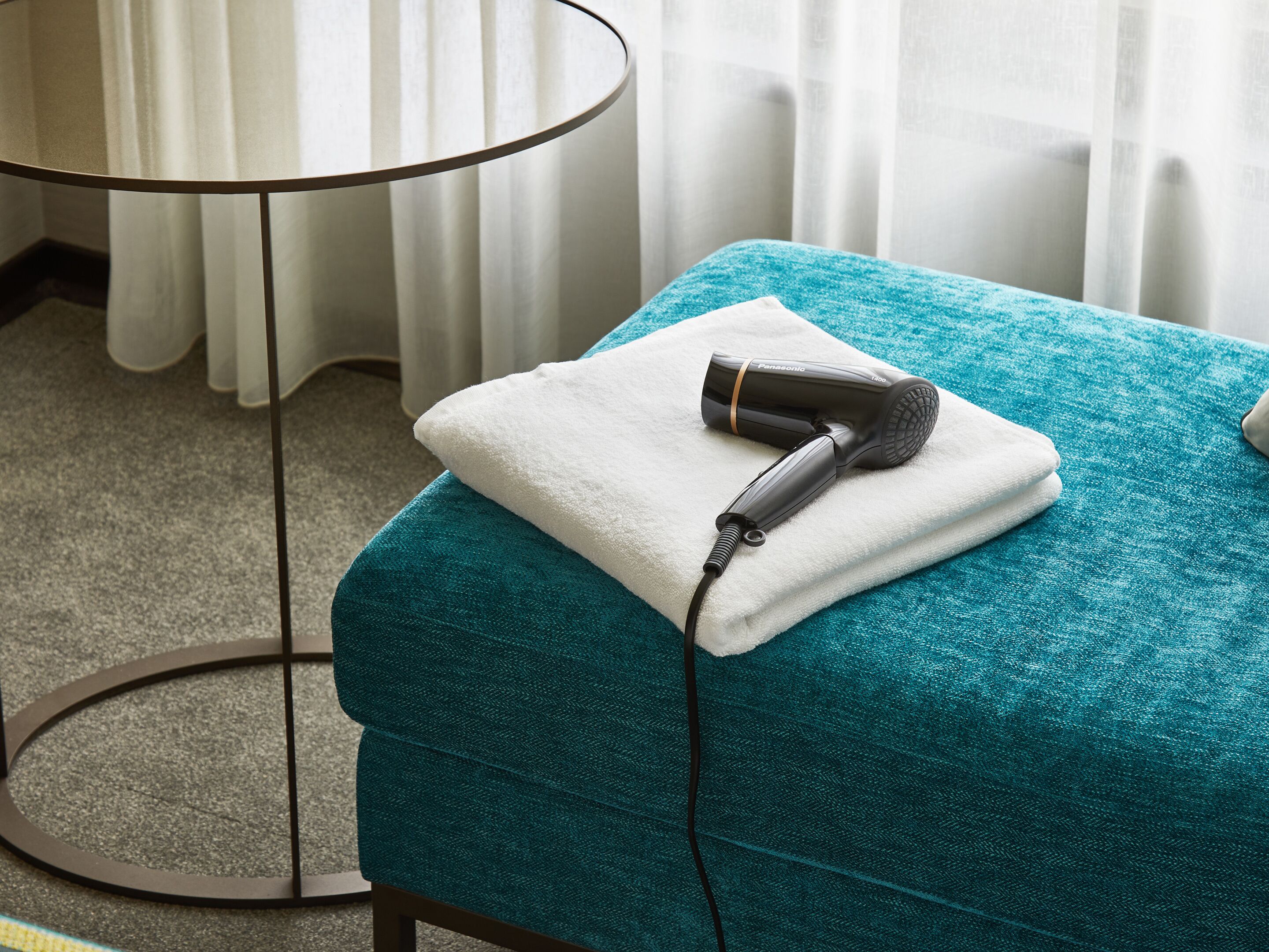A teal-colored massage table with a white towel and a Panasonic hair dryer on it.