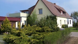 Una casa a due piani con tetto spiovente, un balcone al piano superiore e un giardino curato con diversi arbusti.