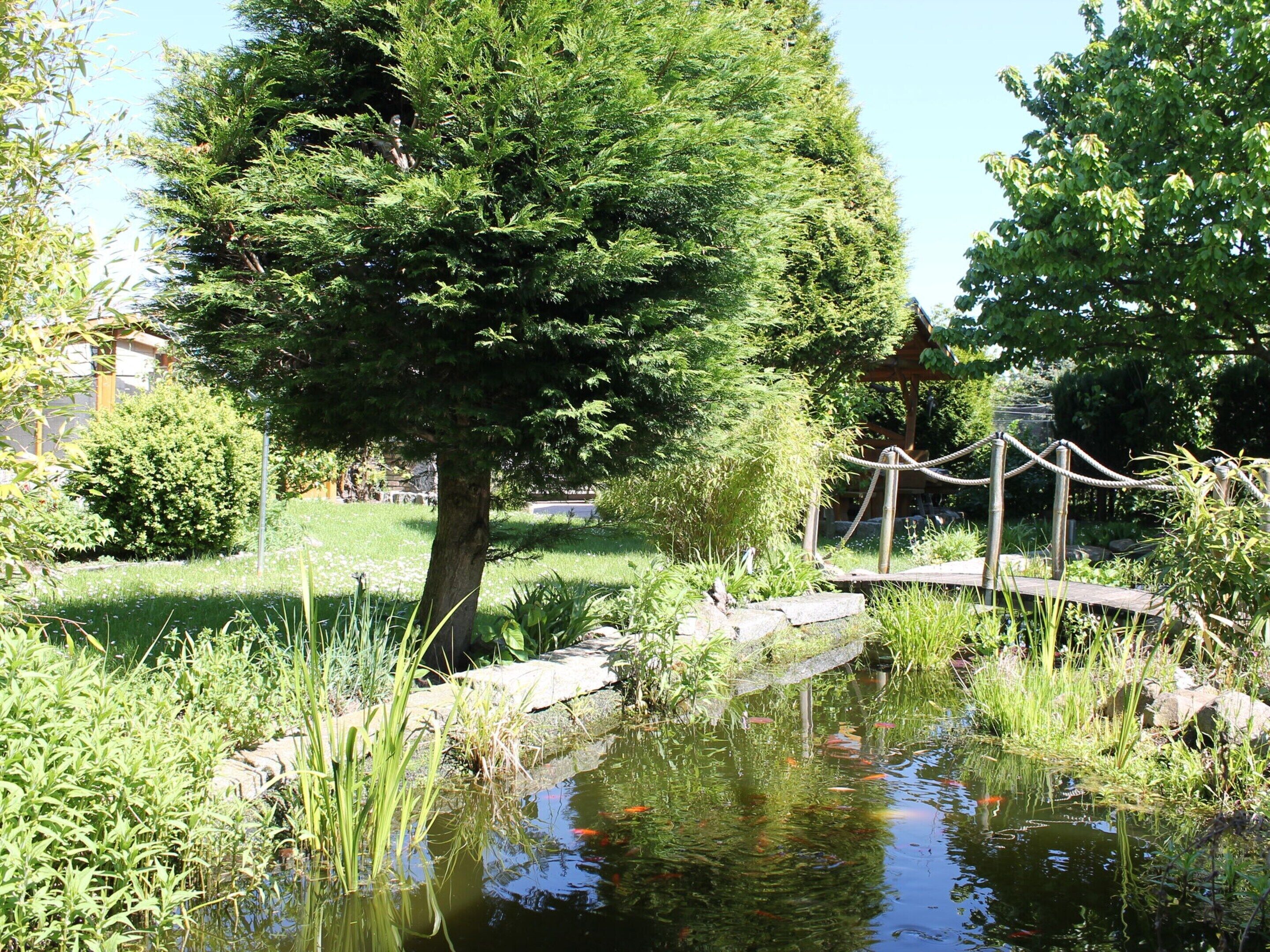 Un jardín tranquilo con un estanque, un puente de madera y abundante vegetación.