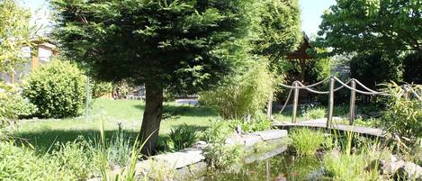 Un jardín tranquilo con un estanque, un puente de madera y abundante vegetación.
