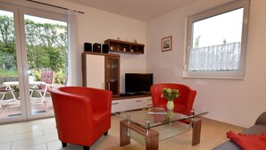 A modern living room with a glass coffee table, red armchairs, a grey sofa, and a TV. - Villa am Meer in Boiensdorf mit Terrasse (Boiensdorf)