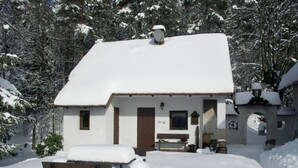 Un petit bâtiment enneigé, avec un banc en bois devant, entouré d’arbres.