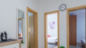 Ein Flur mit Holztüren zu einem Schlafzimmer und einem Badezimmer. An der Wand hängt eine Uhr und auf dem Boden steht ein kleiner Blumentopf.