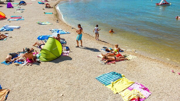 Ein Strand mit badenden Personen, Zelten und Booten.