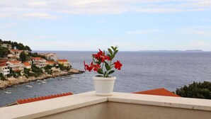 A balcony with a potted red flower, overlooking a coastal town with buildings and boats. - Holiday Home in Korcula With Sea View (Korčula)