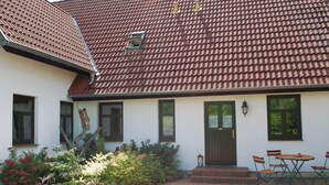 A building with a tiled roof, a front door, and a small garden area with plants and a bench. - Apartment in Dargun With Swimming Pool (Dargun)