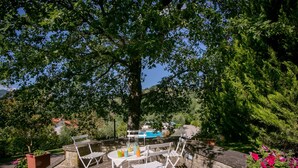 Eine Terrass mit rundem Tisch und weißen Stühlen, umgeben von Steinmauern und Grünpflanzen.