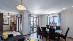 A modern living room with a sofa, a dining table with chairs, a kitchen area, and large windows with curtains. - Modern Villa With Private Pool Near Labin and the Beach (Rasa)