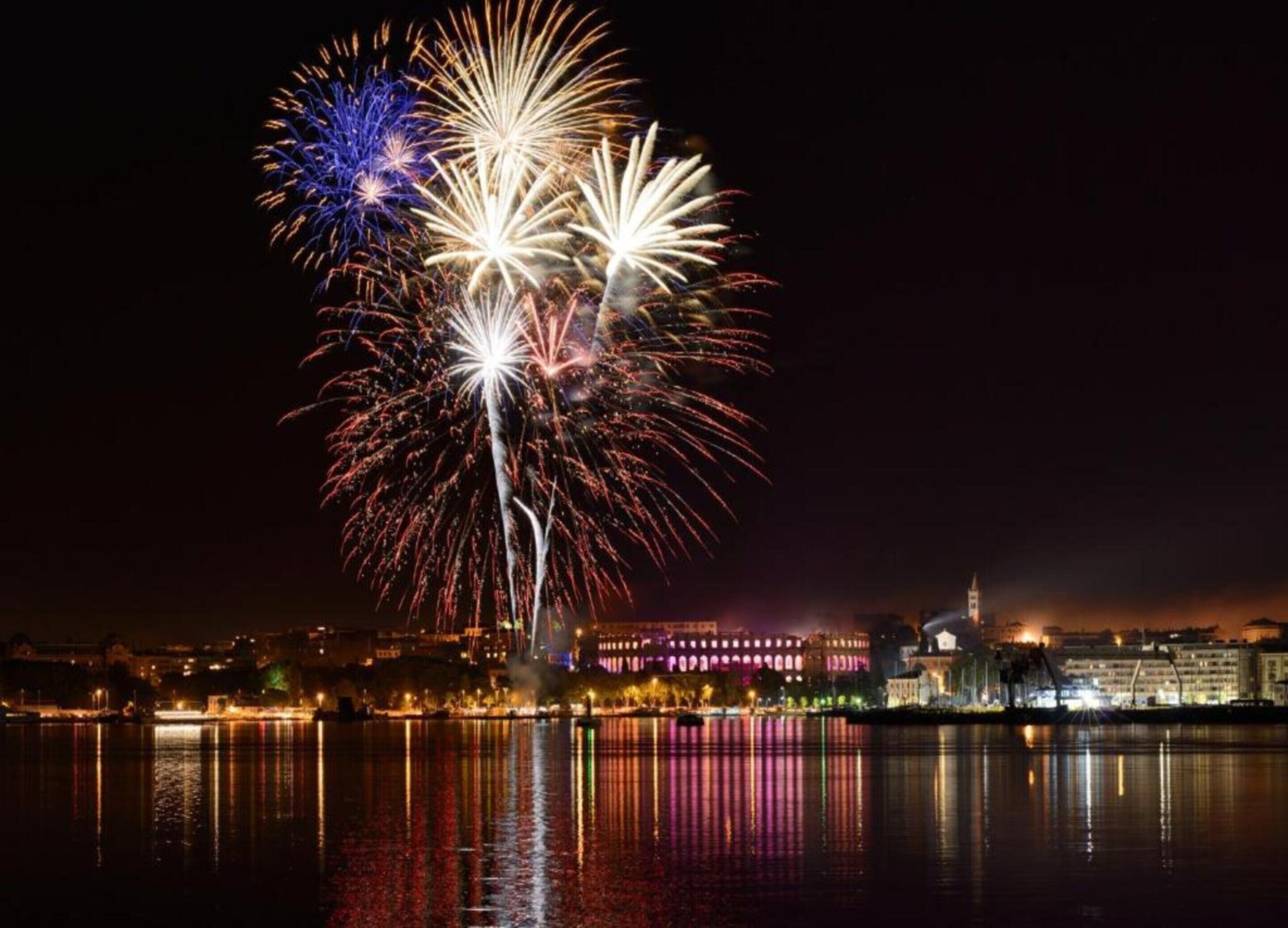 Une vue nocturne d’une ville avec son front de mer et un spectacle de feux d’artifice.