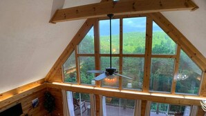 Une pièce dotée d’un plafond en pente, de grandes fenêtres, d’un ventilateur de plafond et offrant une vue sur une terrasse et sur la verdure environnante.