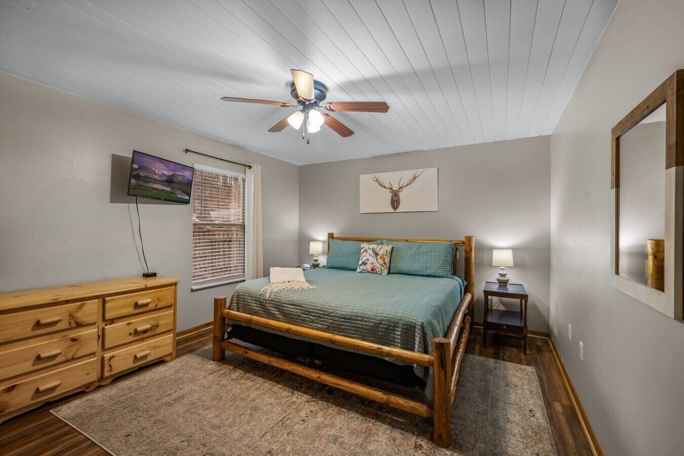 A bedroom with a bed, wooden dresser, ceiling fan, and artwork on the walls.