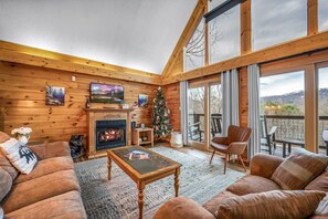 L’intérieur chaleureux d’un chalet en bois avec une cheminée, un sapin de Noël et un balcon offrant une vue imprenable.