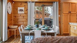L’intérieur d’un chalet en bois, avec une table à manger dressée pour six personnes, une horloge et un tableau encadré accroché au mur.