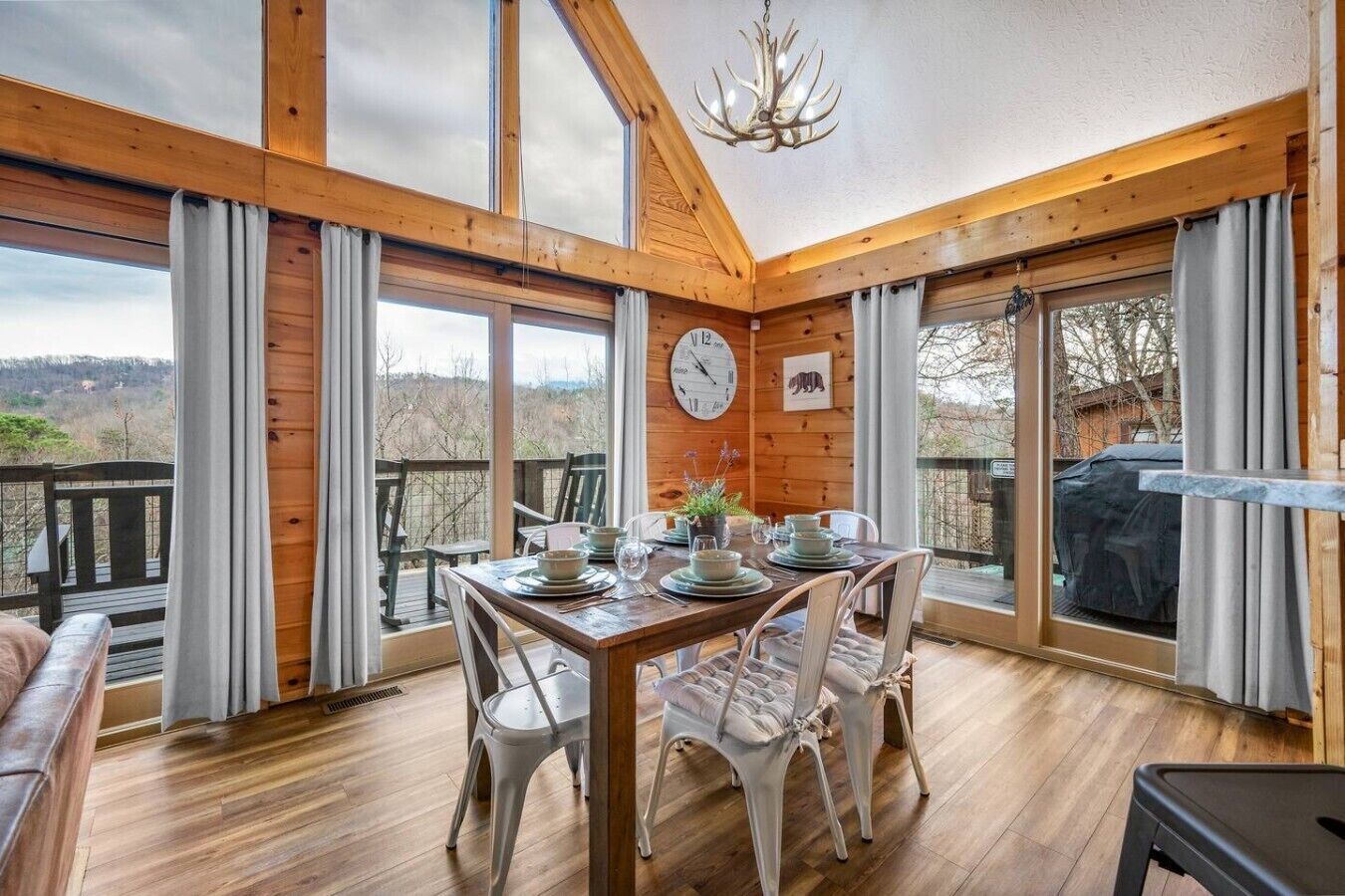 Una cabaña de madera con una mesa de comedor para cuatro, ventanas amplias y un candelabro.